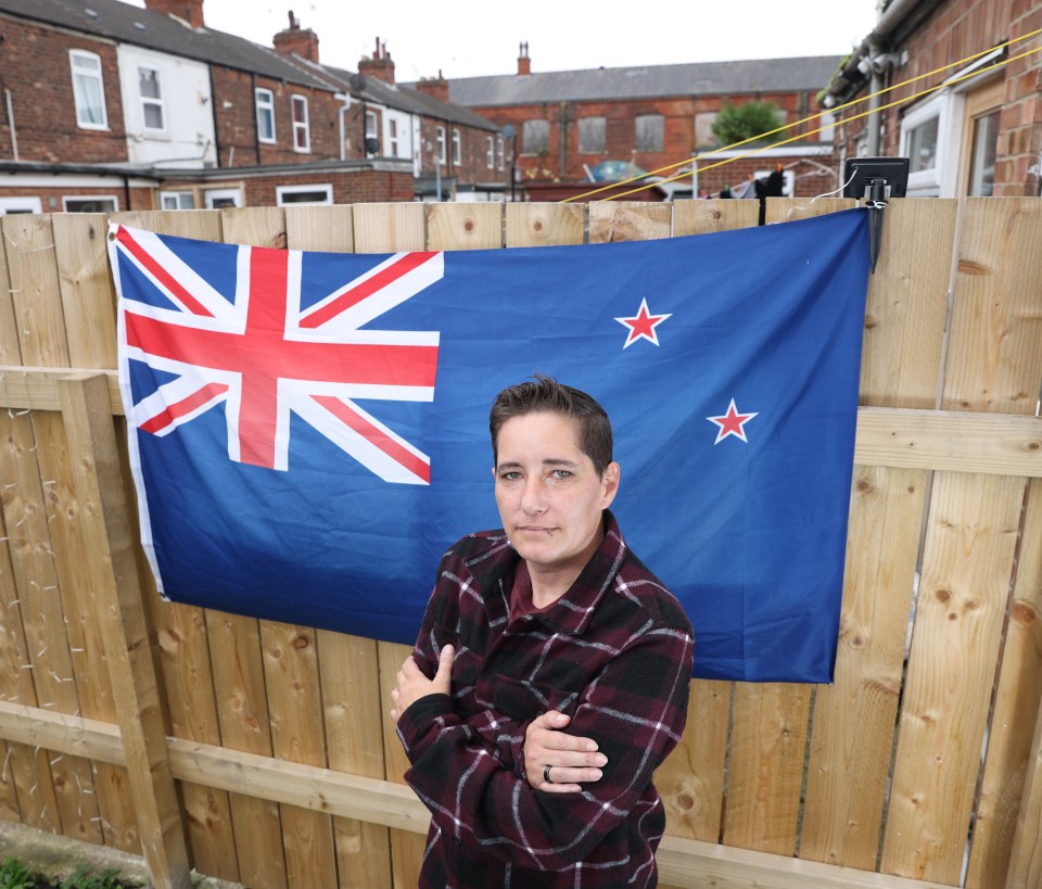 a woman stands in front of a new zealand flag