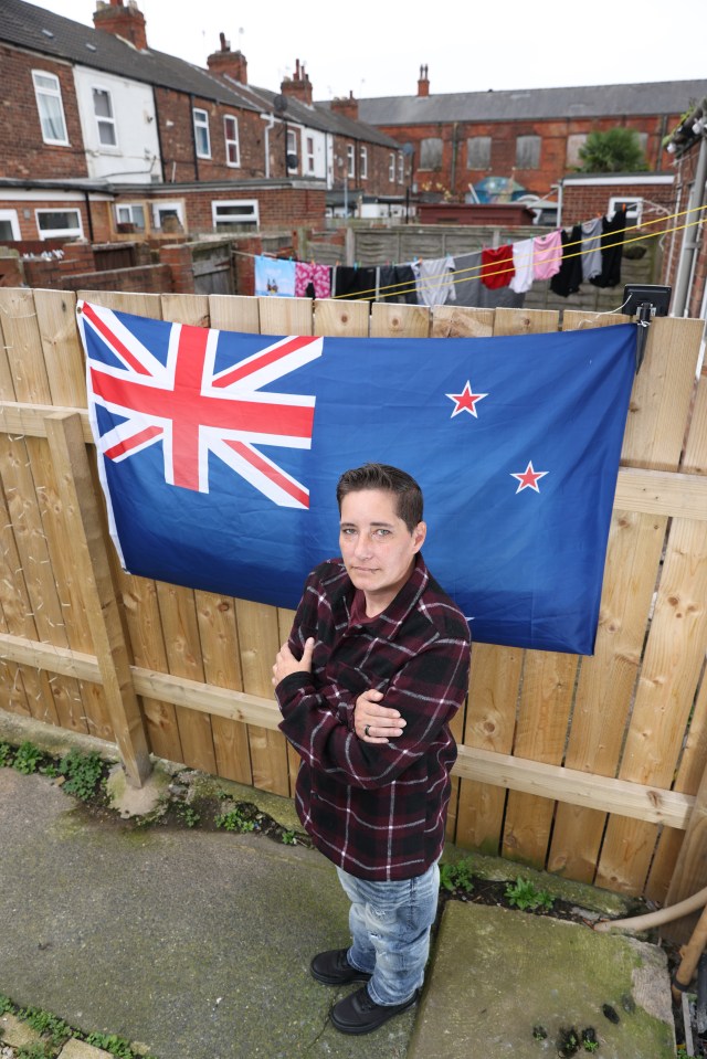 a woman stands in front of a new zealand flag