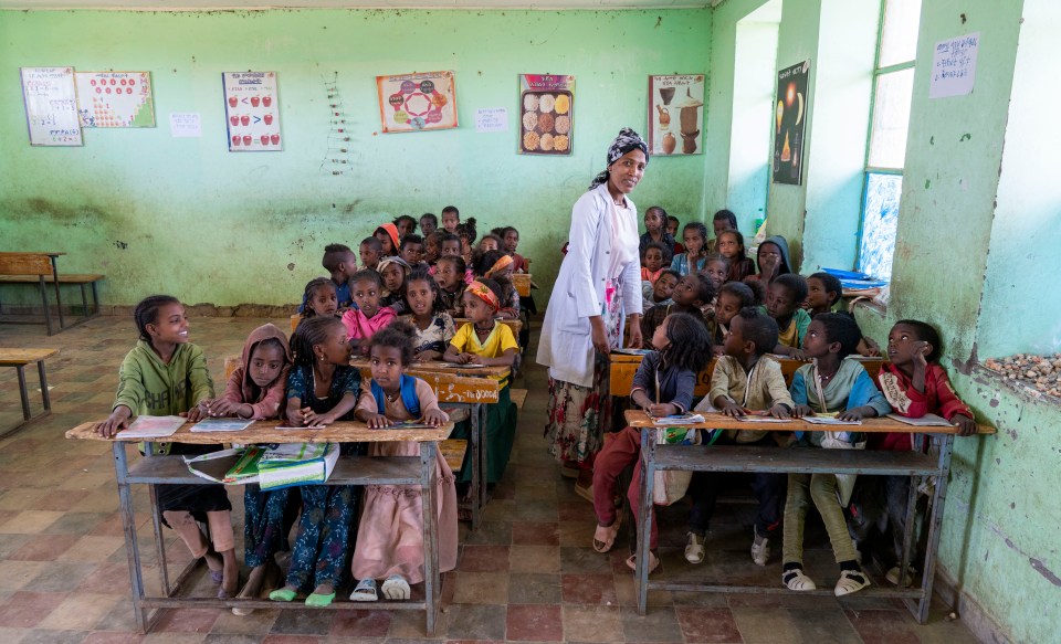 The teacher delivers a lesson to a classroom packed full of eager students