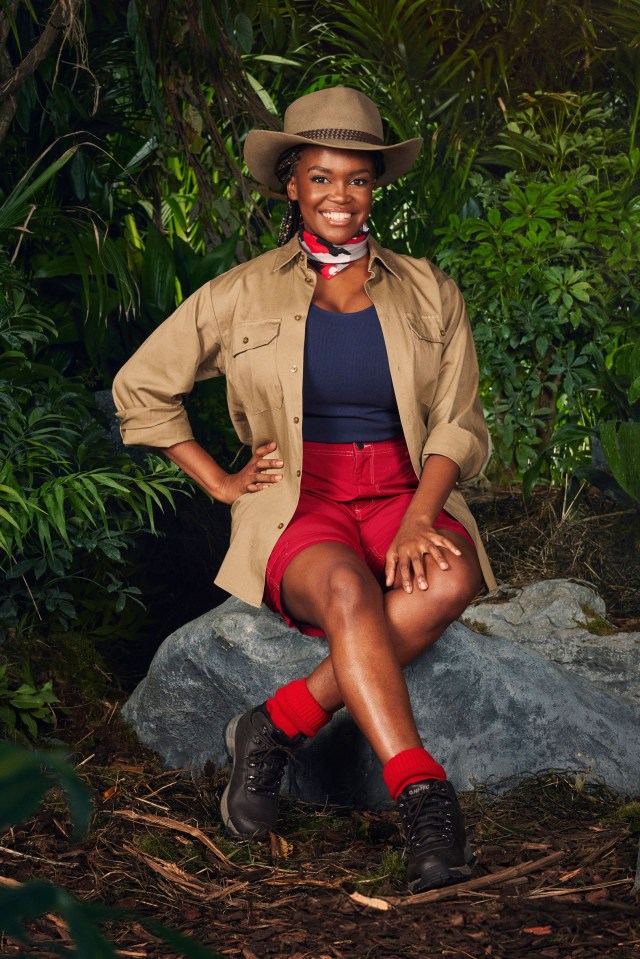 a woman wearing a hat and shorts sits on a rock in the jungle