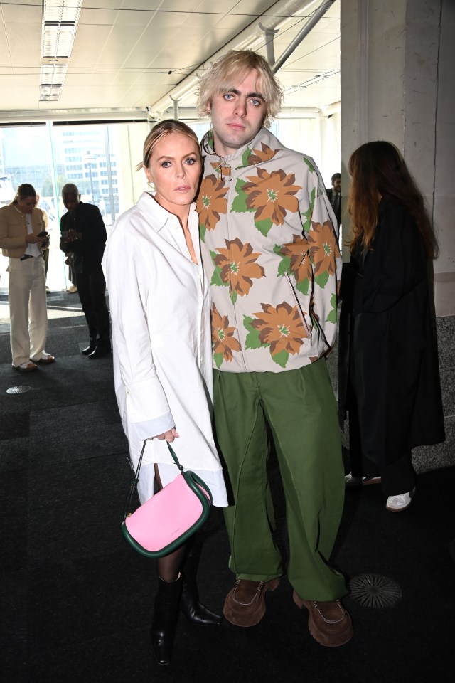 a woman holding a pink purse stands next to a man in a floral jacket