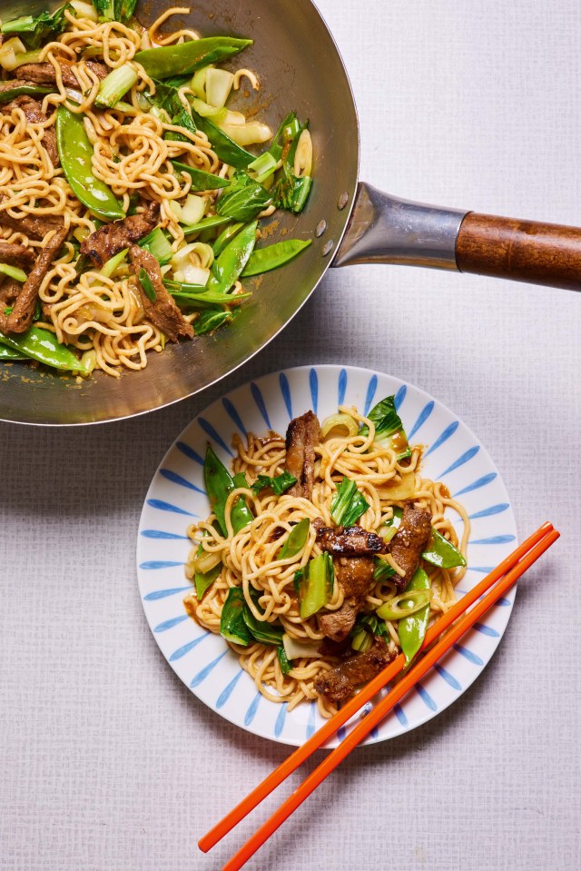 a plate of noodles with meat and vegetables next to a wok