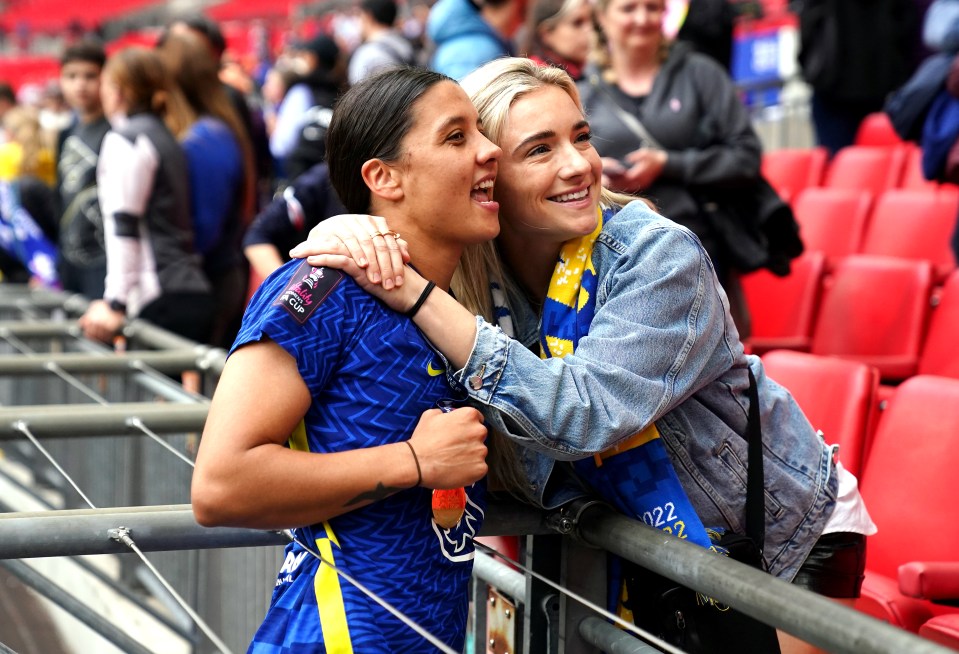 two women hugging in a stadium with one wearing a shirt that says ' chelsea ' on it