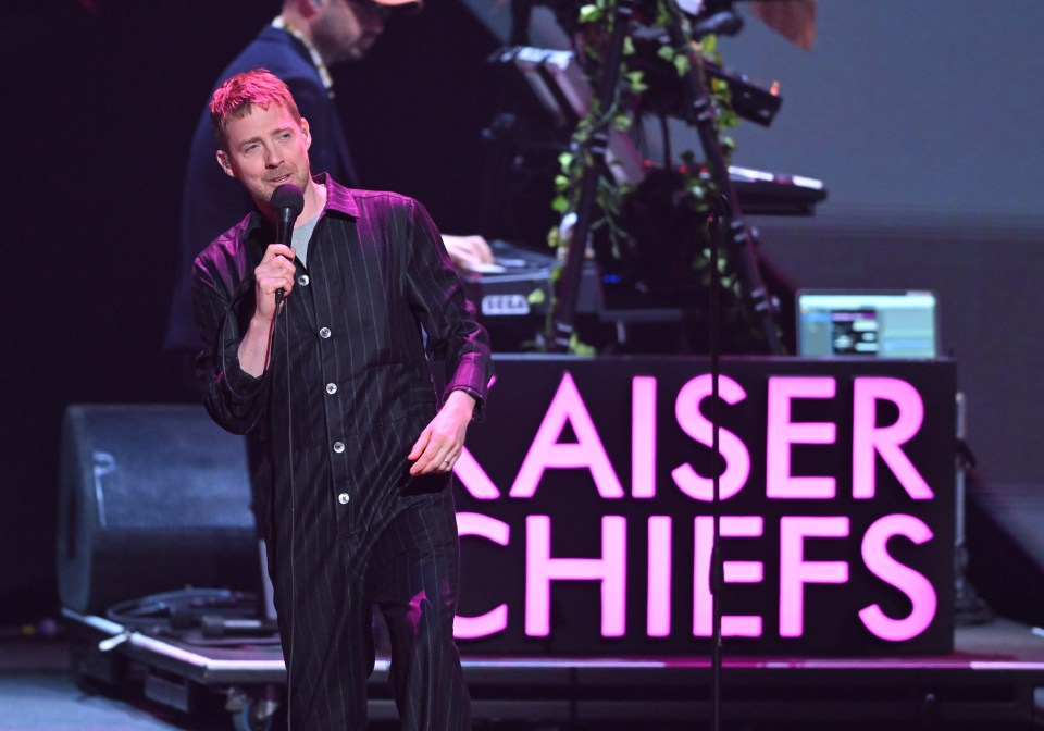 a man singing in front of a sign that says kaiser chiefs