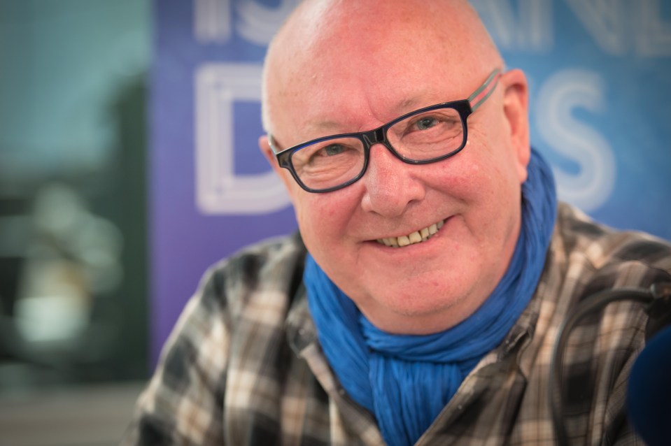 a bald man wearing glasses and a blue scarf smiles for the camera