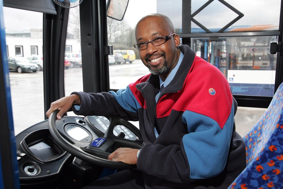 a man in a red and blue jacket is driving a bus