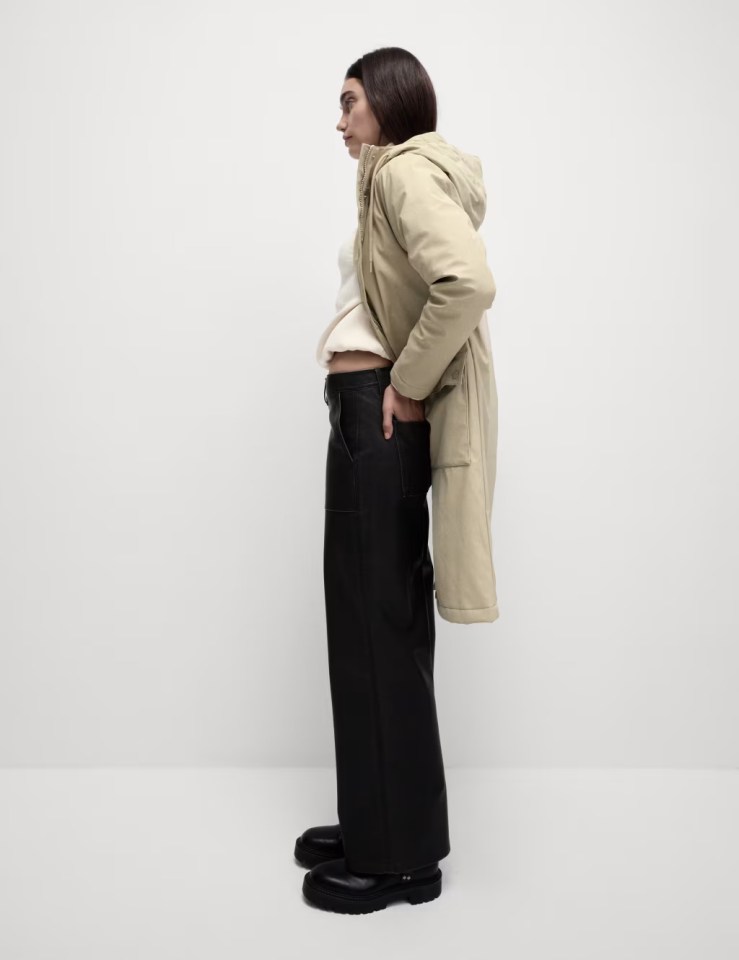 a woman wearing a beige coat and black pants