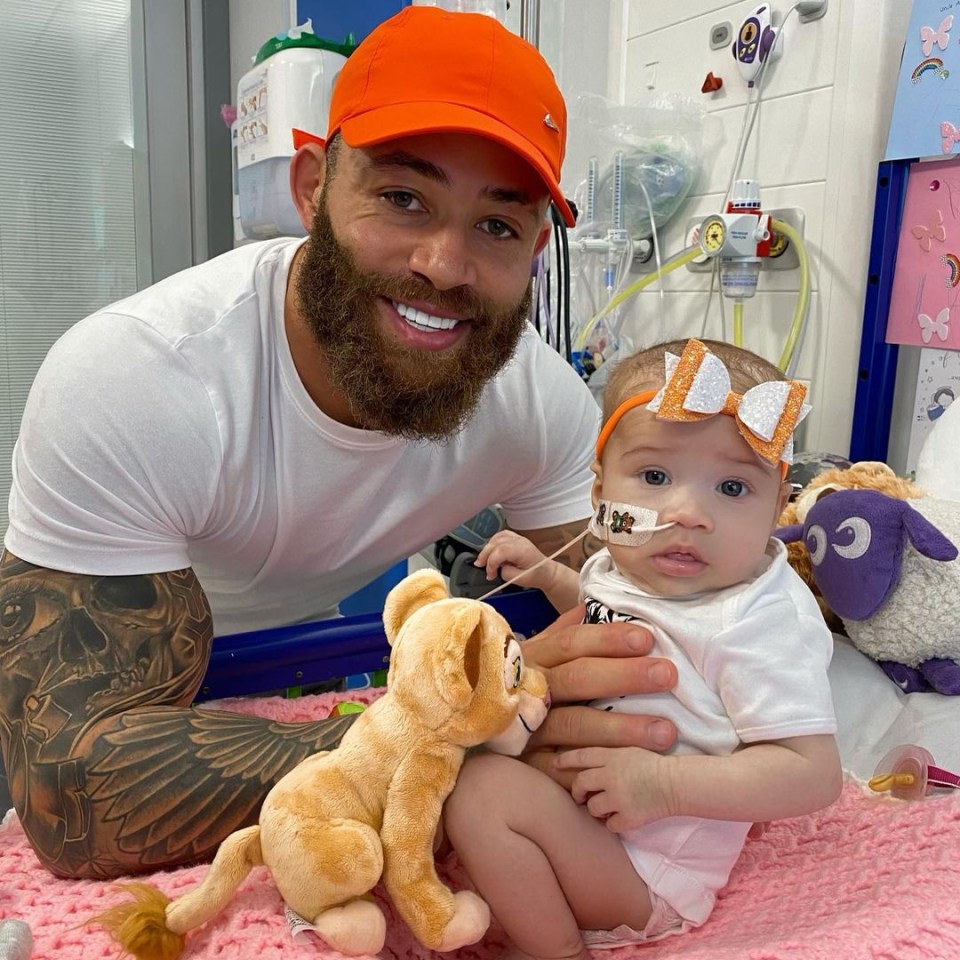 a man in an orange hat holds a baby in a hospital room