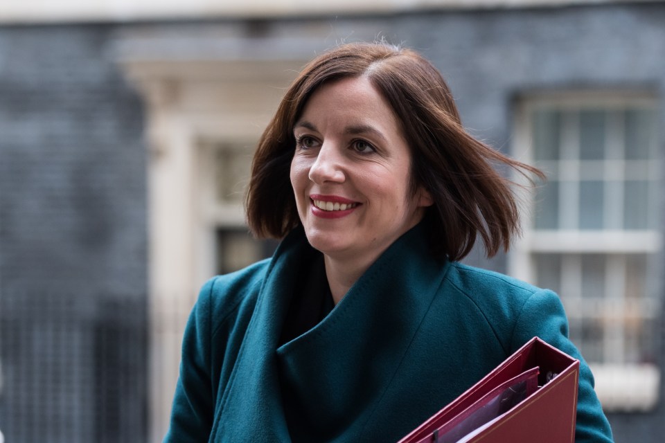 a woman in a green coat is smiling and holding a red folder