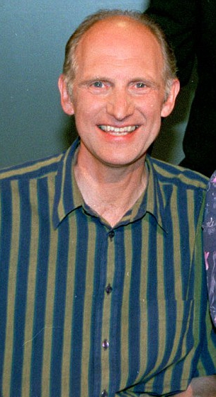 a man wearing a blue and green striped shirt smiles for the camera