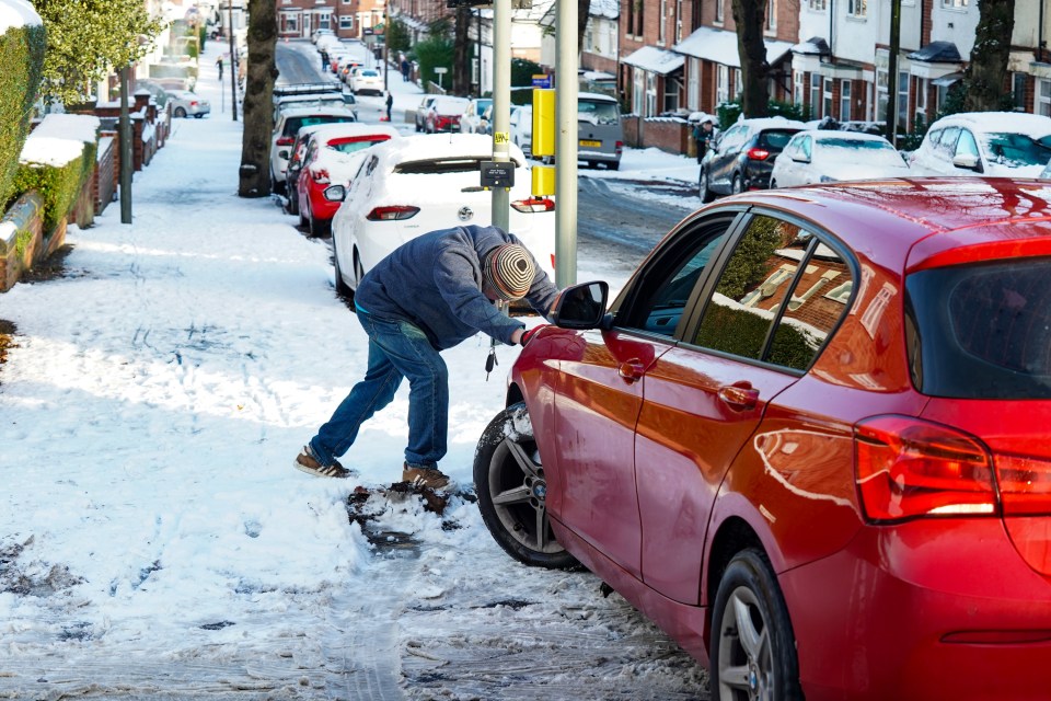 a man is shoveling snow from a red car