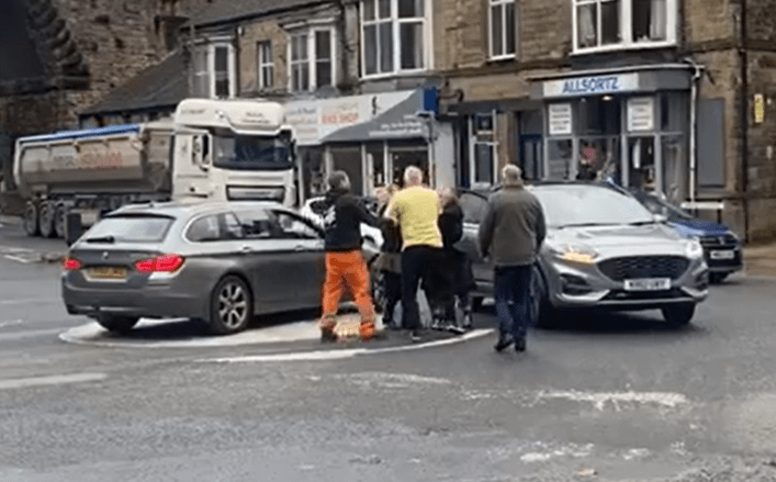 a group of people are standing around a car that has crashed into a truck .