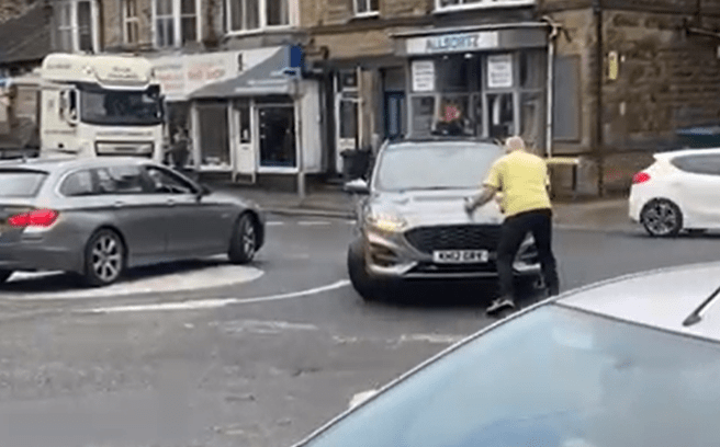 a man in a yellow shirt is cleaning the windshield of a car .