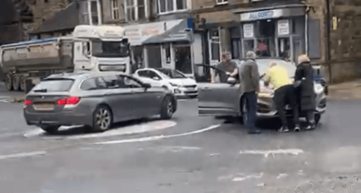 a group of people are standing around a car at an intersection .