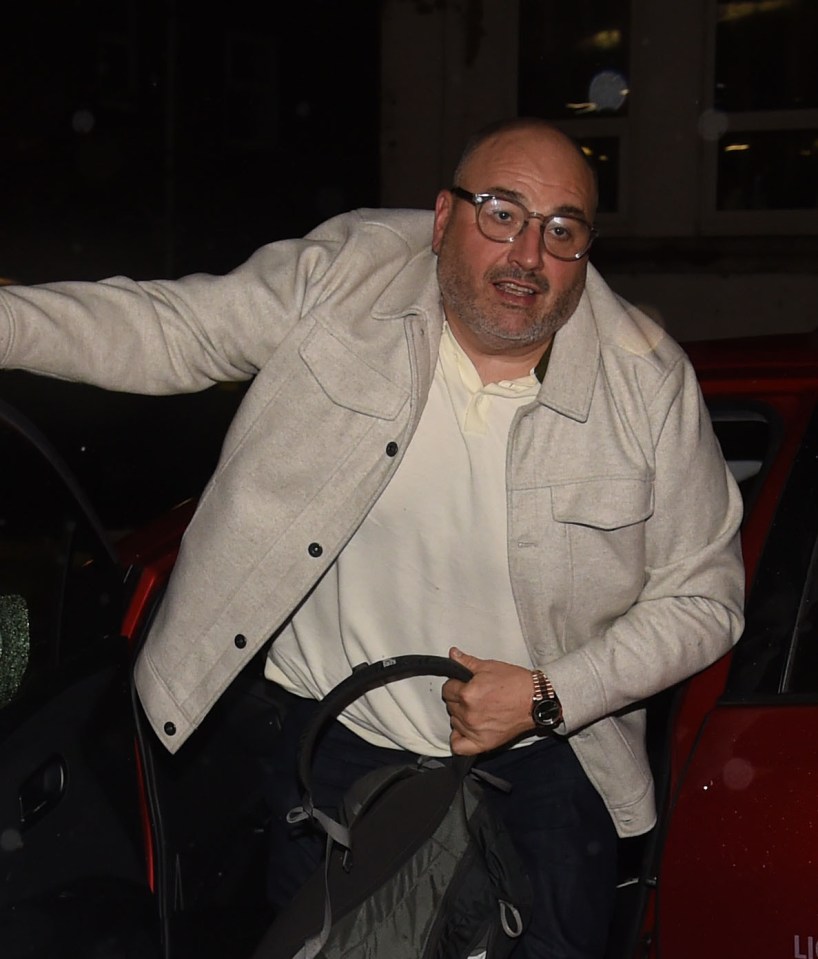 a bald man wearing glasses and a white jacket is getting out of a red car