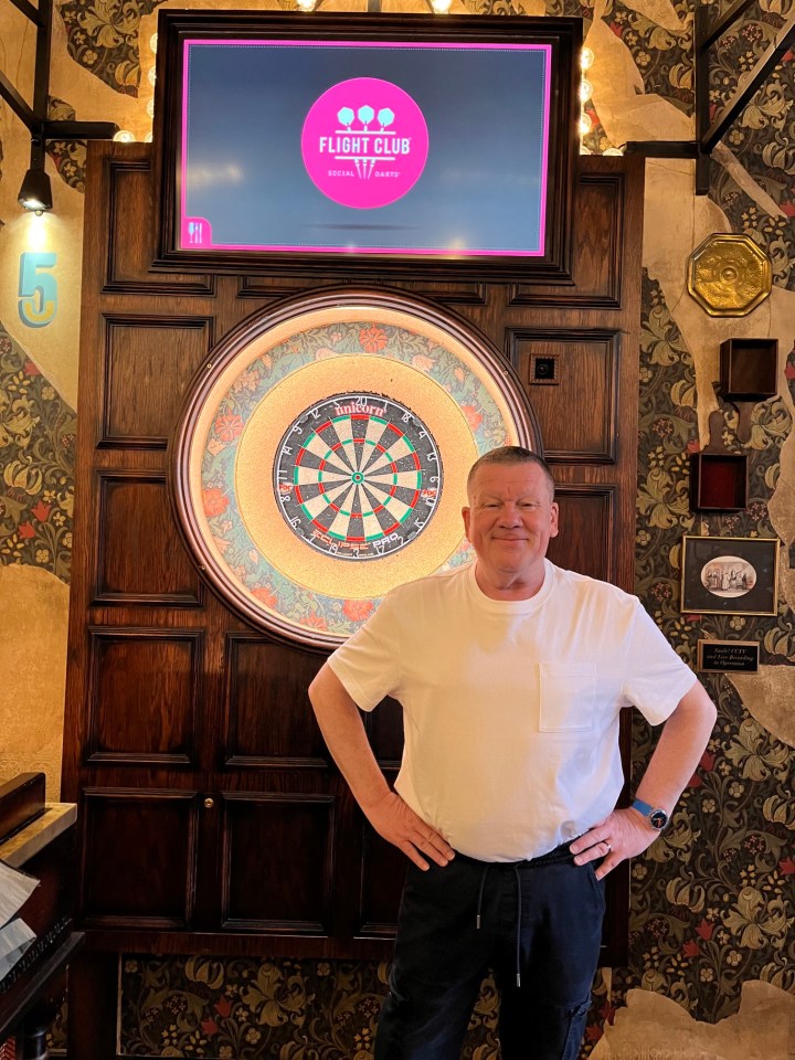 a man stands in front of a dart board that says flight club