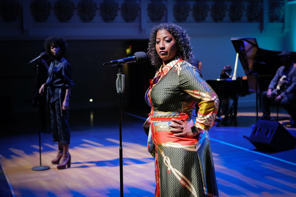 a woman singing into a microphone with her hands on her hips