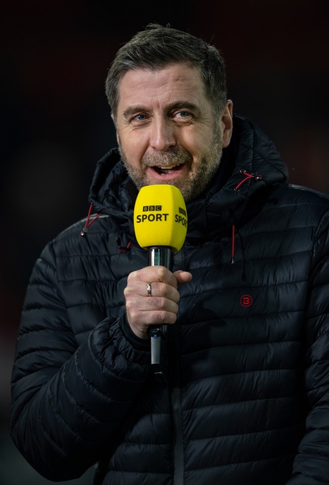 a man in a black jacket is holding a yellow bbc sport microphone