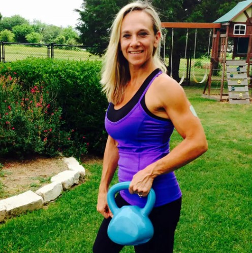 a woman in a purple tank top is holding a blue kettlebell