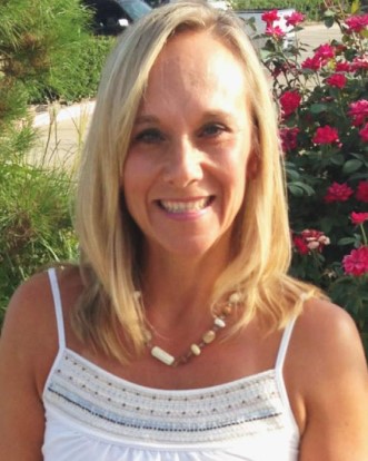 a woman wearing a white tank top and a necklace smiles for the camera