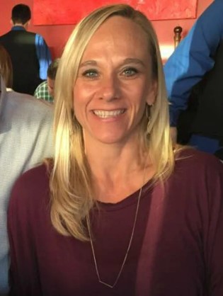 a woman in a purple shirt and necklace is smiling for the camera .