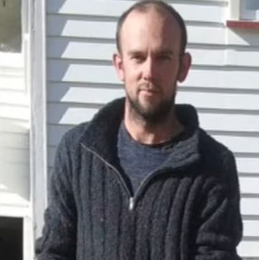 a man with a beard is wearing a sweater and standing in front of a white house .