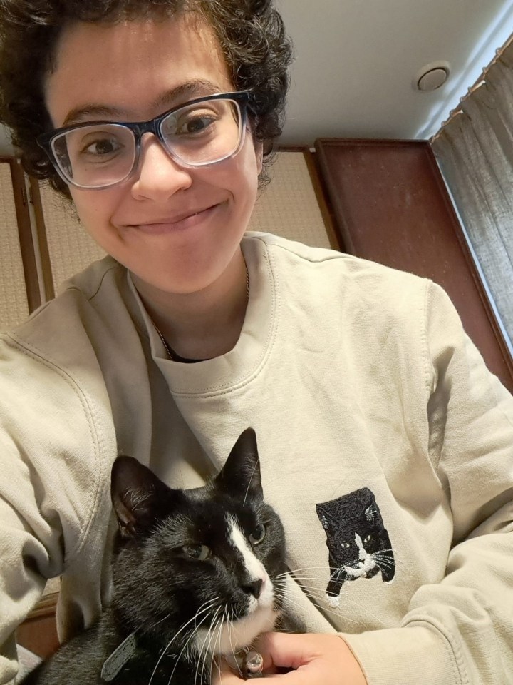 a woman wearing glasses holds a black and white cat