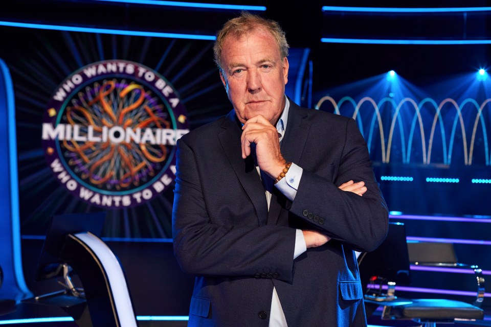 a man in a suit stands in front of a sign that says who wants to be a millionaire