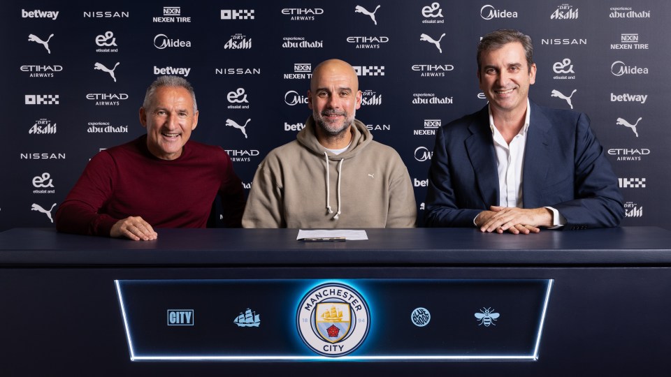 three men sitting in front of a manchester city sign