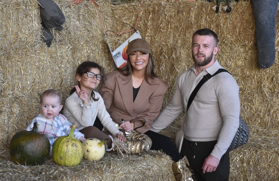 a family sits on a bale of hay with pumpkins