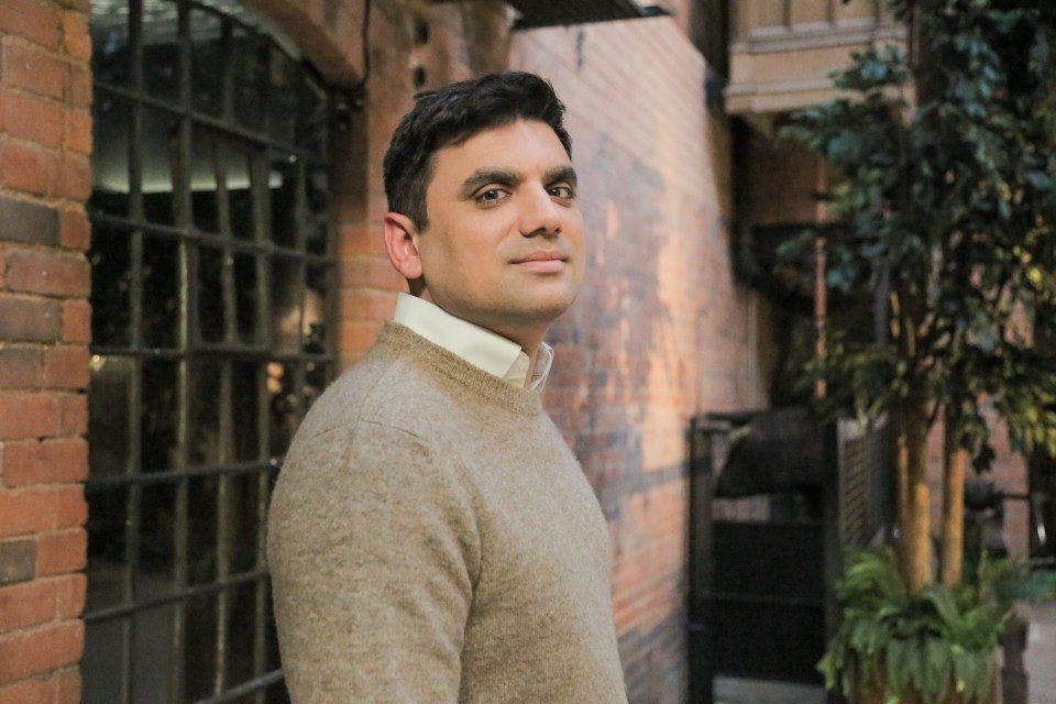 a man in a tan sweater stands in front of a brick building