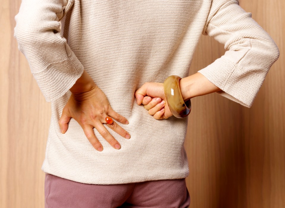 a woman wearing a bracelet is holding her back in pain