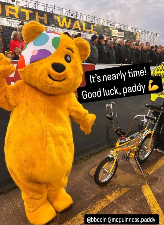 a yellow teddy bear mascot standing next to a yellow bicycle