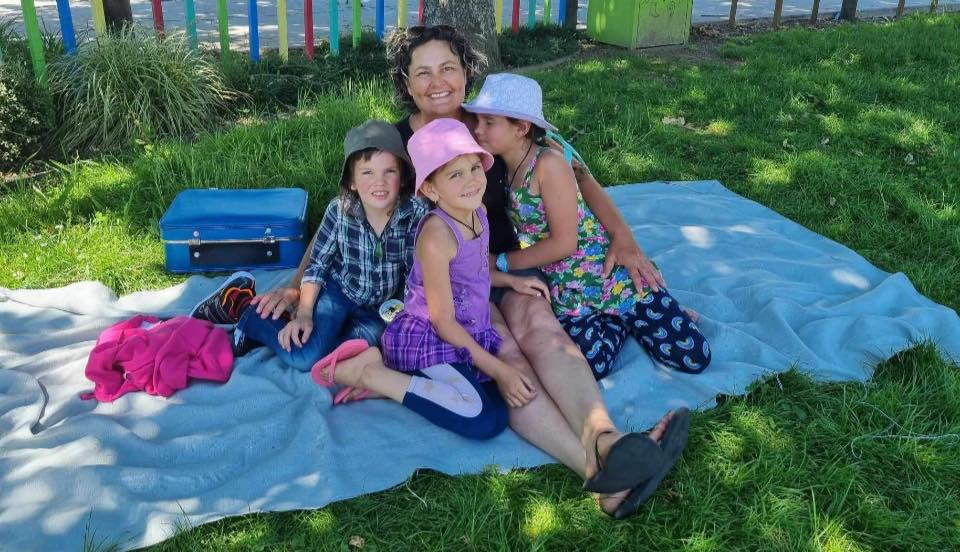 a woman sits on a blanket with three children and a blue suitcase