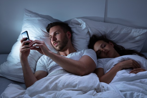 a man and a woman are laying in bed looking at their phones