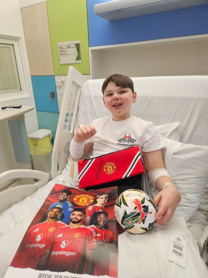 Boy in hospital bed with signed Manchester United gifts.