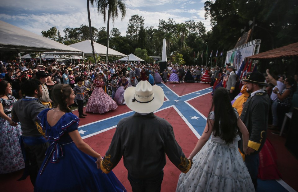 People in traditional outfits hold hands between dances at the annual Festa Confederada, or Confederate Party