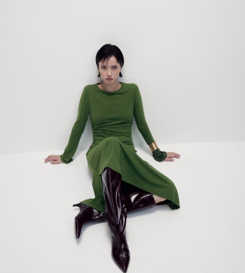 Woman in green dress and dark boots sitting on the floor.