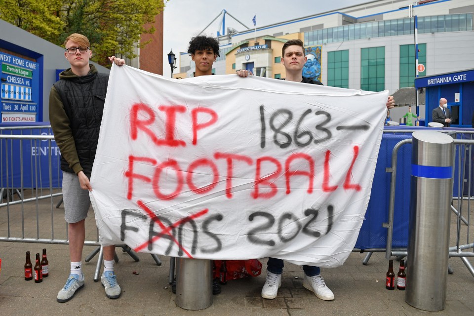 Three football fans hold a banner that reads "RIP FOOTBALL FANS 1863-2021," protesting against the European Super League.