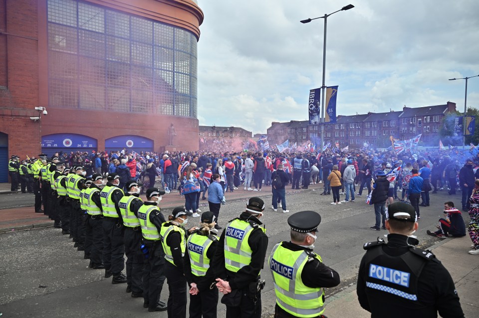 Police officers monitor Rangers fans celebrating a Scottish Premiership title win.