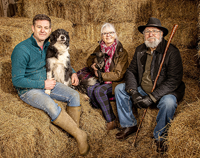 Matt Baker with his parents and two dogs in a hay barn.