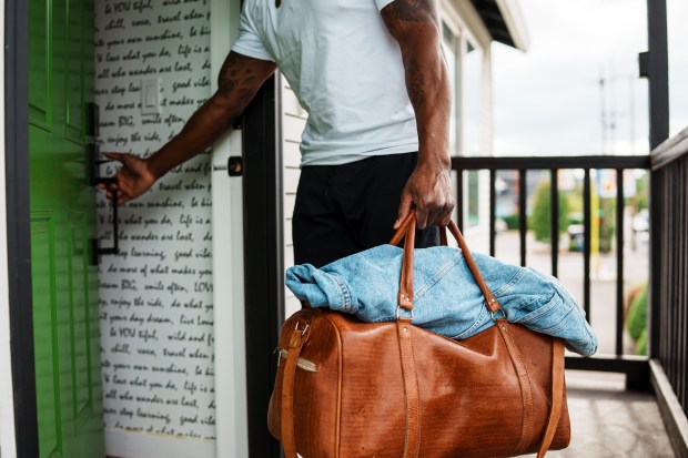 Man leaving home with a brown leather duffel bag.