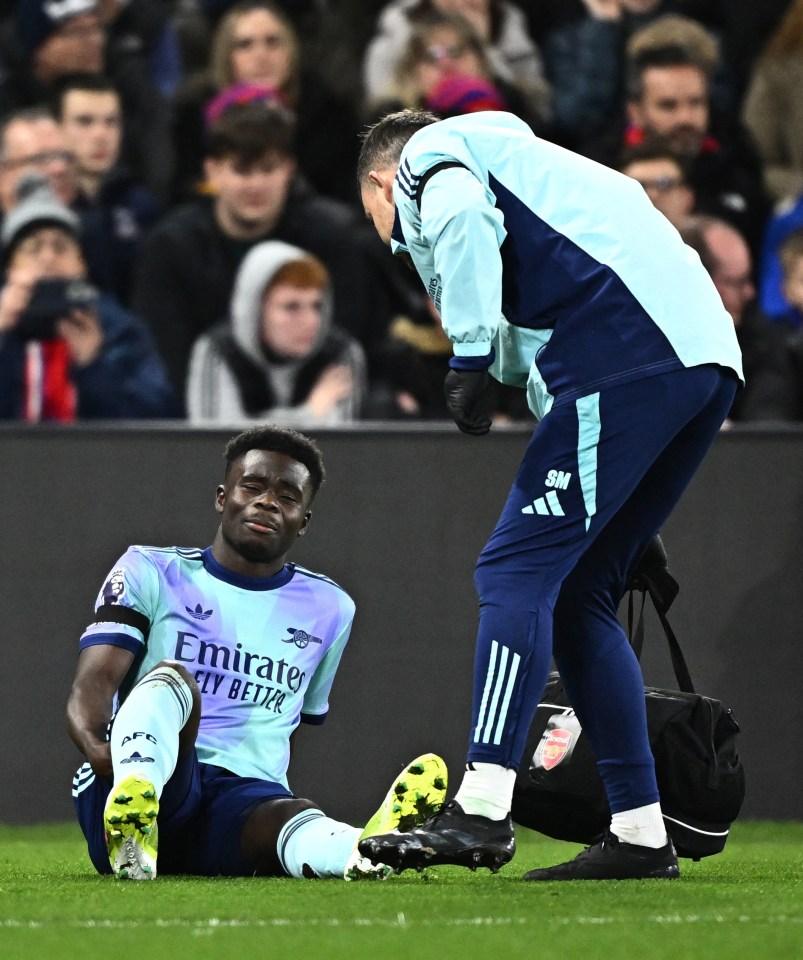 Injured Arsenal's Bukayo Saka receiving medical attention on the field.