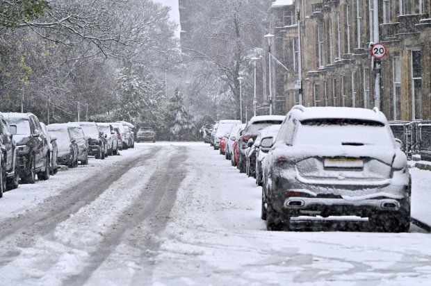 Snow-covered cars and pedestrians on a city street during a heavy snow shower.