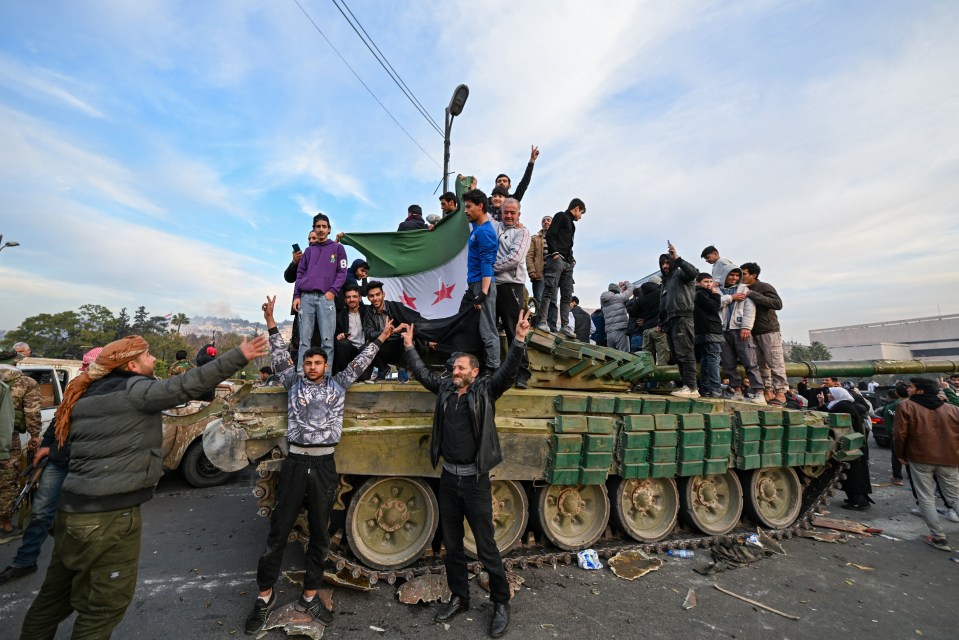 People celebrating on a damaged tank, holding a flag.