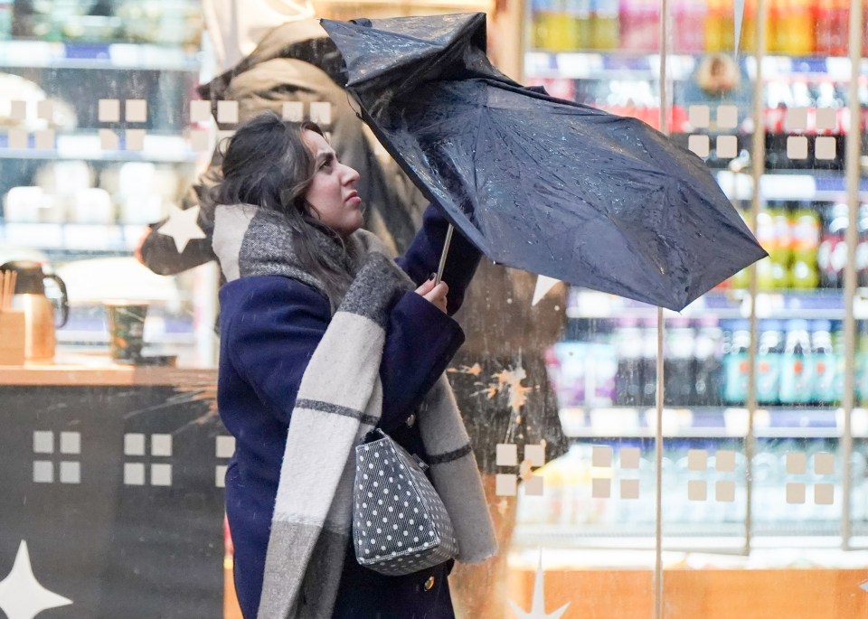 A woman struggles to hold her umbrella in Manchester as parts of the UK are hit by heavy rain and strong winds