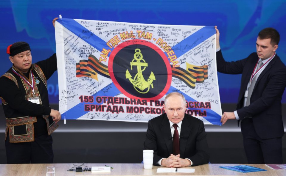 Putin smiles as men hold a Marine banner behind him