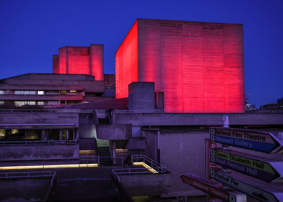 The National Theatre in London, illuminated in red at night.