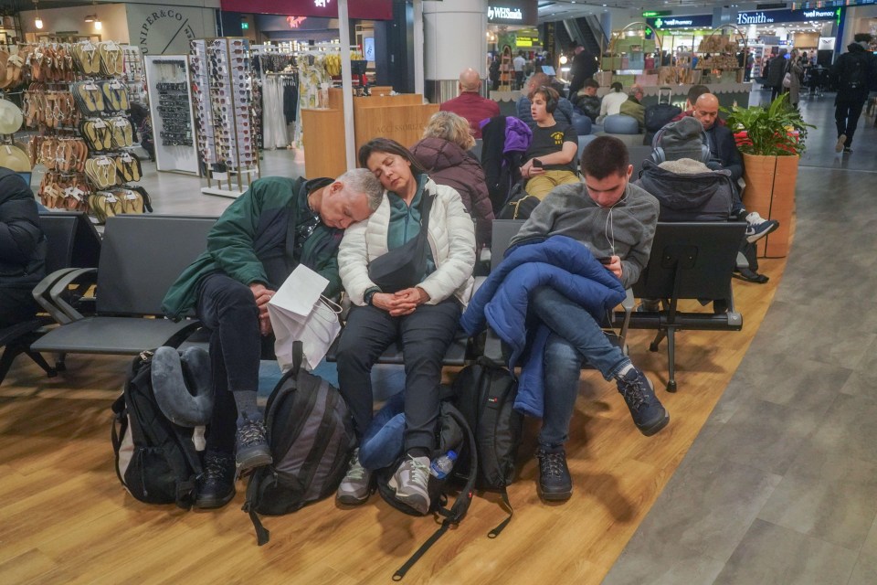 Passengers sleeping and using phones in an airport departure lounge.