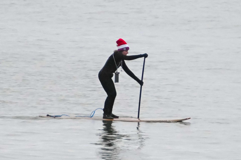 Person paddleboarding on calm water wearing a Santa hat.